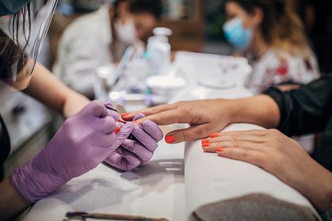 Eine Frau lackiert die Fingernägel einer anderen Frau im Nagelstudio