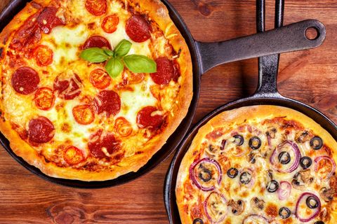 Eine Pfannenpizza mit Salami neben einer mit Oliven und Zwiebeln