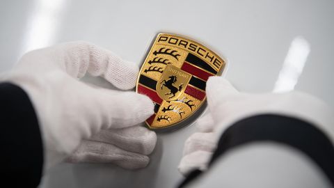 Eine Mitarbeiterin der Porsche AG hält in der Produktion ein Porsche-Emblem auf die Motorhaube eines Porsche Taycan.