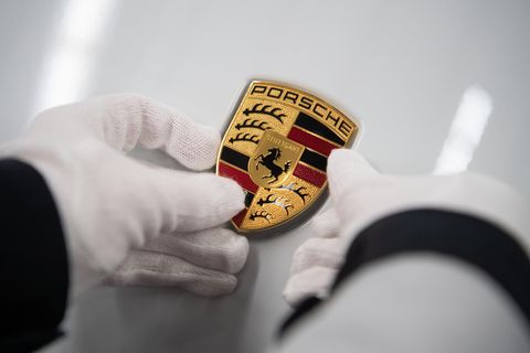 Eine Mitarbeiterin der Porsche AG hält in der Produktion ein Porsche-Emblem auf die Motorhaube eines Porsche Taycan.