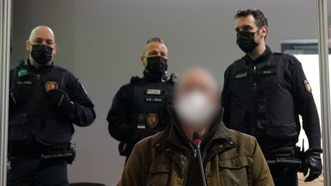 Hartmut F. im Gerichtssaal in Kiel – bewacht von drei Polizisten