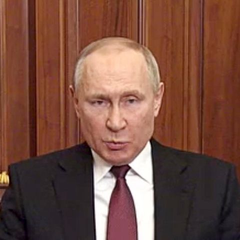 Wladimir Putin Ein älterer weißer Mann mit Halbglatze sitzt in schwarzem Anzug und dunkelroter Krawatte an einem Holztisch und gestikuliert