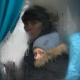 Hinter einem beschlagenen Busfenster schaut ein Junge mit blauen Augen durch eine freigewischte Stelle.