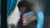 Hinter einem beschlagenen Busfenster schaut ein Junge mit blauen Augen durch eine freigewischte Stelle.