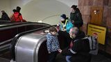 Neben einer Rolltreppe ist ein Mann mit Halbglatz in die Hocke gegangen, um mit einem Jungen auf Augenhöhe zu sprechen.