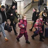 Ein Mann und eine Frau gehen mit Gepäck und zwei Mädchen in rosa gemusterten Schneeanzügen durch eine Metro-Station