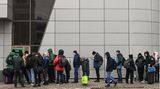 Vor einem grünen Geldautomaten stehen Menschen in Winterkleidung Schlange