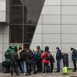 Vor einem grünen Geldautomaten stehen Menschen in Winterkleidung Schlange