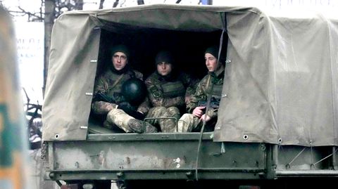 Von der Ladefläche eines militärgrünen Lastwagens schauen drei Soldaten in Uniform aus der hinten aufgeschlagenen Plane