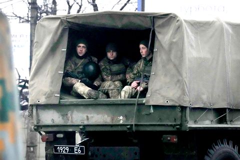 Von der Ladefläche eines militärgrünen Lastwagens schauen drei Soldaten in Uniform aus der hinten aufgeschlagenen Plane