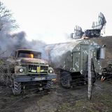 Ein brennender Militärlaster steht neben zwei Radarschüsseln auf einem Hügel