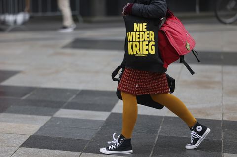 Eine Närrin geht am Donnerstag in Köln mit einer Tasche mit der Aufschrift "Nie wieder Krieg" über die Domplatte.