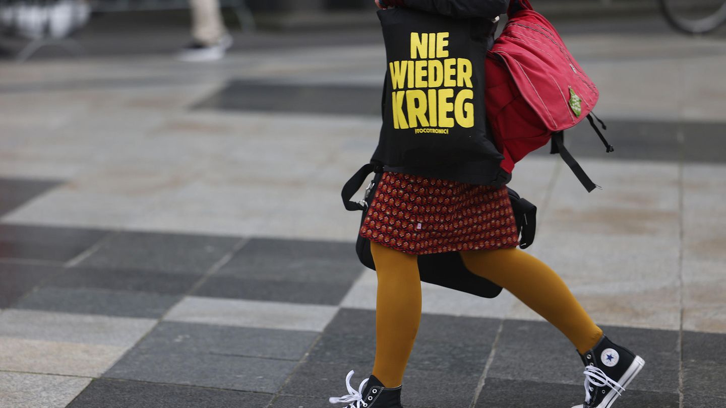 Eine Närrin geht am Donnerstag in Köln mit einer Tasche mit der Aufschrift "Nie wieder Krieg" über die Domplatte.