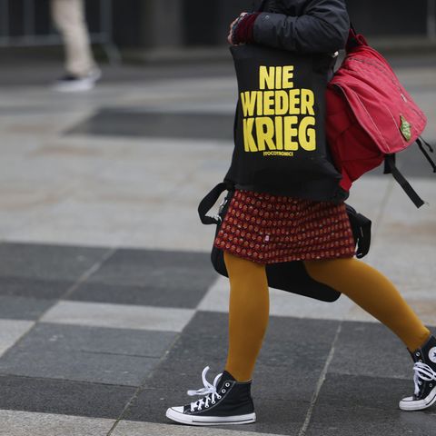 Eine Närrin geht am Donnerstag in Köln mit einer Tasche mit der Aufschrift "Nie wieder Krieg" über die Domplatte.