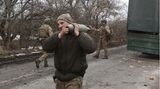 Ein Soldat trägt auf der linken Schulter eine graue Granate. Im Hintergrund steht ein Militär-Lkw
