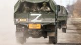 Drei Soldaten mit Gewehren im Anschlag sitzen auf der Ladefläche eines Militär-Lkw und schauen nach hinten