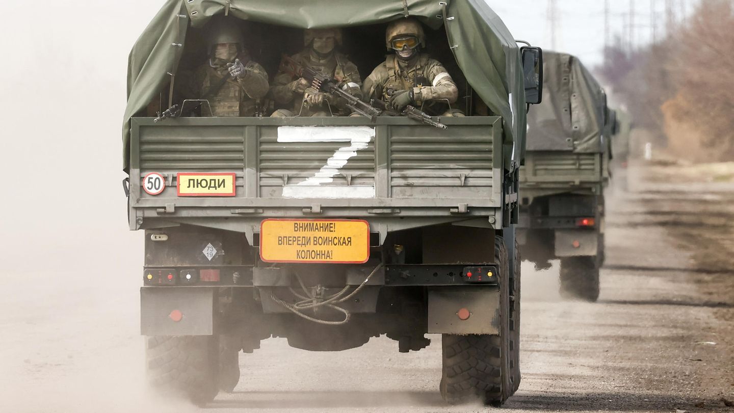 Drei Soldaten mit Gewehren im Anschlag sitzen auf der Ladefläche eines Militär-Lkw und schauen nach hinten