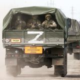 Drei Soldaten mit Gewehren im Anschlag sitzen auf der Ladefläche eines Militär-Lkw und schauen nach hinten