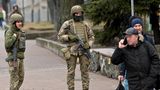Soldaten in voller Kampfausrüstung stehen auf einer Straße, während zwei Männer in Winterkleidung von ihnen weggehen