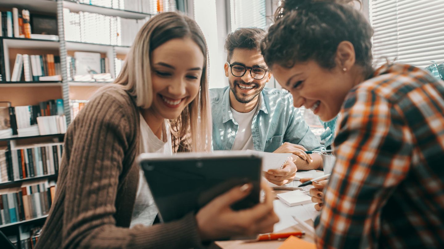 Drei Student:innen sitzen in der Bibliothek und schauen auf ein Chromebook-Tablet.
