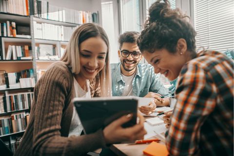 Drei Student:innen sitzen in der Bibliothek und schauen auf ein Chromebook-Tablet.