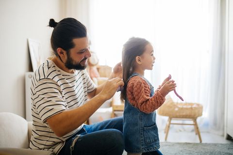 Ein Vater kämmt seiner kleinen Tochter die Haare, während sie ihm etwas erzählt