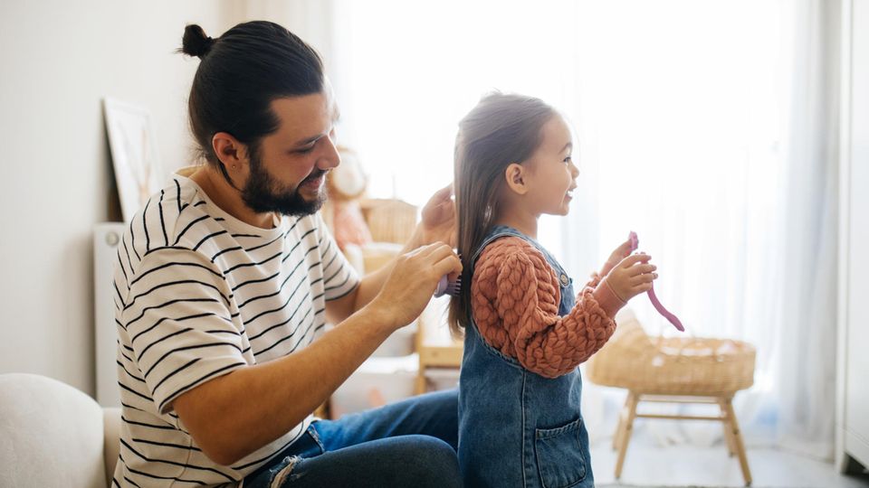 Ein Vater kämmt seiner kleinen Tochter die Haare, während sie ihm etwas erzählt