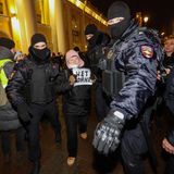 Eine ältere Frau hält immer noch ihren Schild mit der Aufschrift "Nein zum Krieg", als sie abgeführt wird