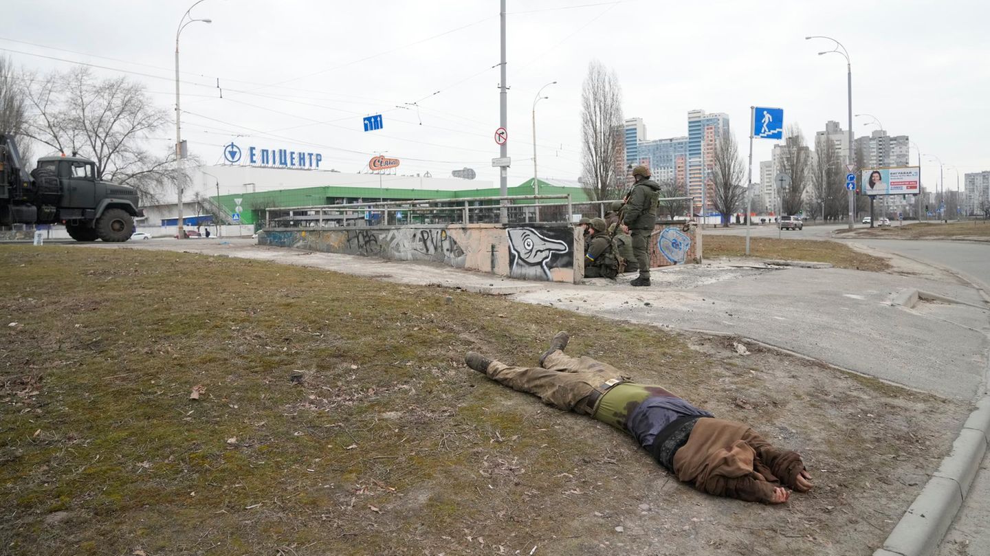 Die Leiche eines getöteten, mutmaßlich russischen Soldatens liegt auf dem Boden, während Soldaten der ukrainischen Armee in eine Unterführung gehen.