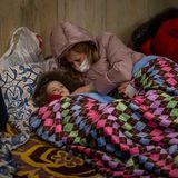 Eine Frau mit Kind wärmt sich unter einer Decke auf dem kalten Boden der U-Bahn-Station.