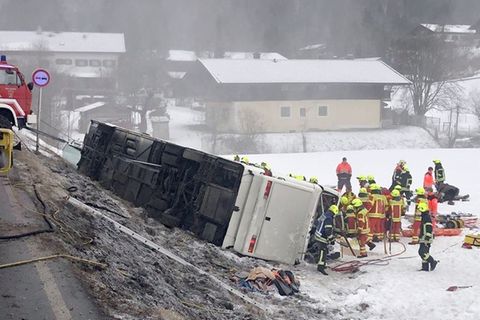 Einsatzkräfte der Feuerwehr stehen auf am Ortsausgang von Inzell neben einem umgekippten Reisebus am Straßenrand