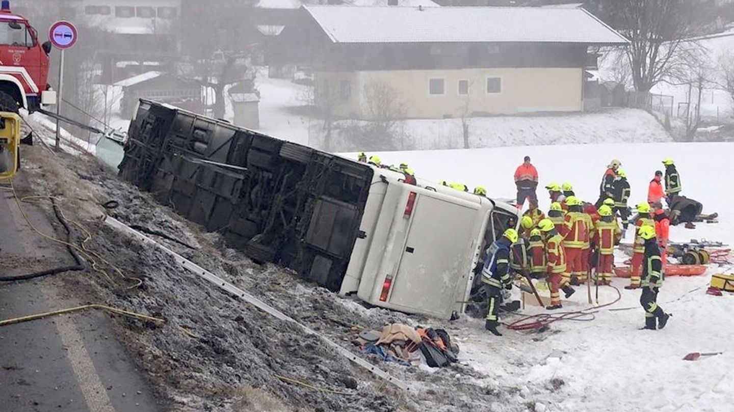 Einsatzkräfte der Feuerwehr stehen auf am Ortsausgang von Inzell neben einem umgekippten Reisebus am Straßenrand