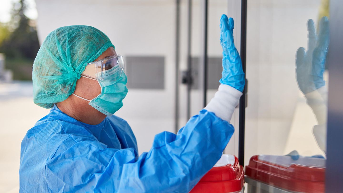 Organspende: Eine Medizinerin in Schutzkleidung hebt bei einem Organtransport vor einem Klinikeingang die Hand für Einlass