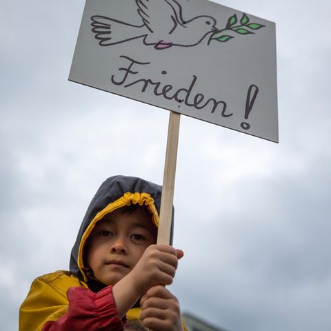 Kleiner Junge hält ein Plakat mit einer Taube und der Aufschrift "Frieden!"