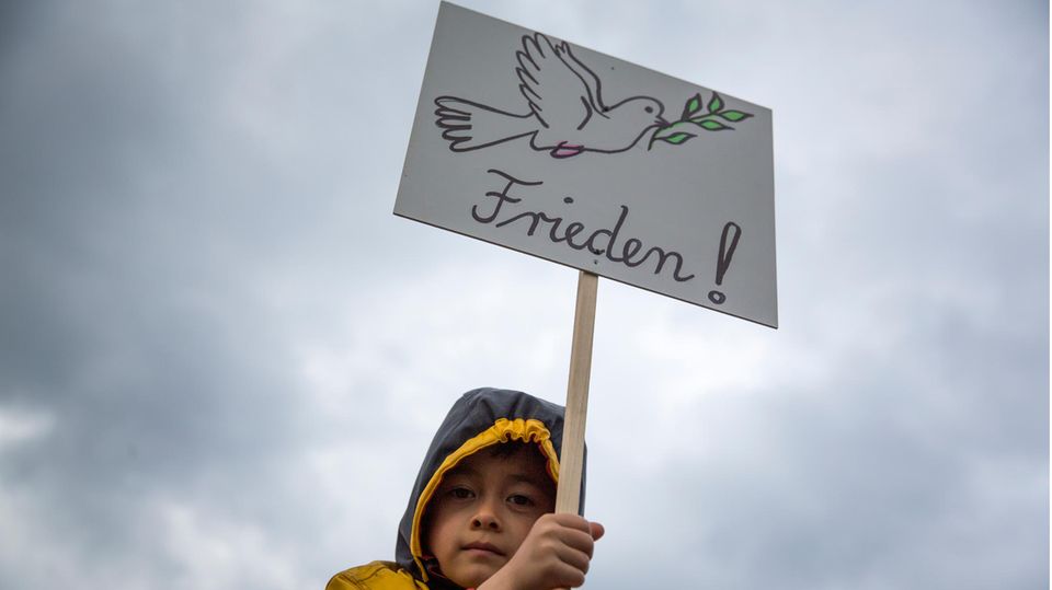 Kleiner Junge hält ein Plakat mit einer Taube und der Aufschrift "Frieden!"