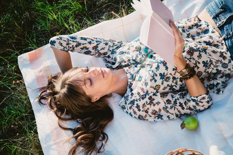 Eine Frau liegt auf einer Decke im Gras und liest
