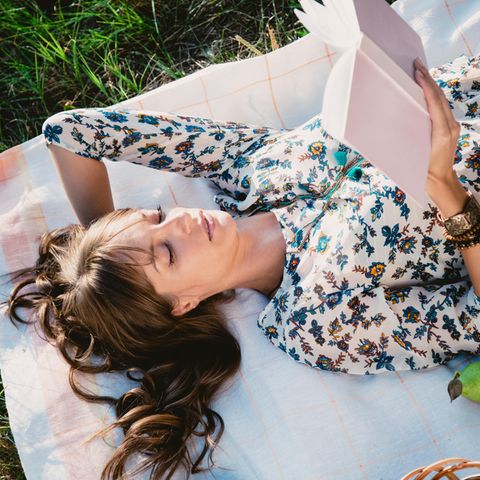Eine Frau liegt auf einer Decke im Gras und liest