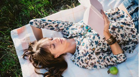 Eine Frau liegt auf einer Decke im Gras und liest