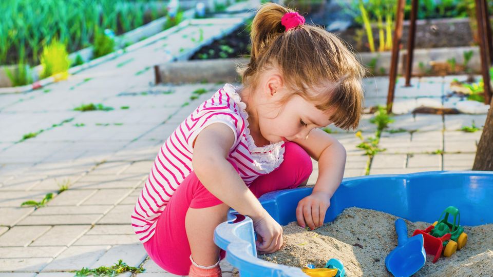 Ein Mädchen spielt mit einer Sandmuschel im Garten