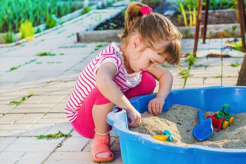 Ein Mädchen spielt mit einer Sandmuschel im Garten