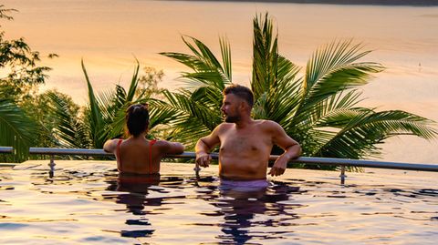 Ein Paar badet im Pool und schaut in den Sonnenuntergang