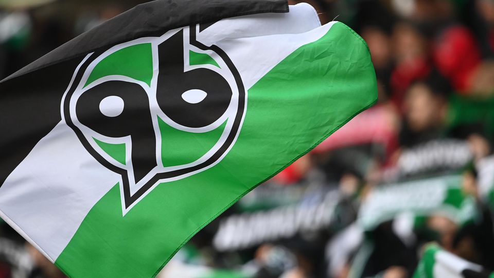 Eine Flagge mit dem Logo von Hannover 96 ist vor der Fantribüne zu sehen
