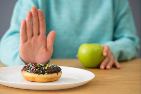 Fastenzeit Verzicht auf Süßes: Frau schiebt Donut weg und isst einen Apfel