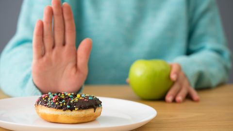 Fastenzeit Verzicht auf Süßes: Frau schiebt Donut weg und isst einen Apfel