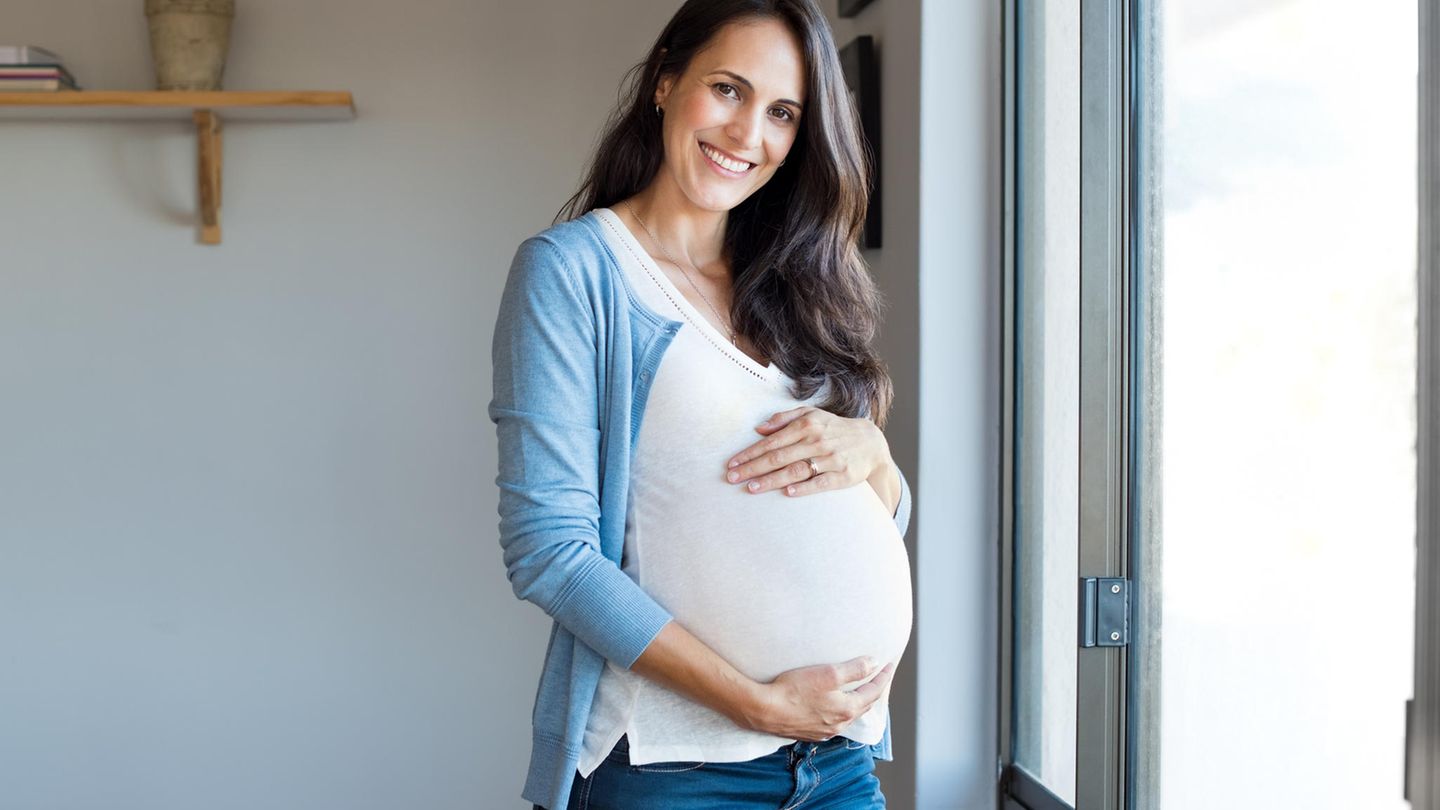 Eine schwangere Frau Mitte 30 lächelt und streichelt über ihren Bauch