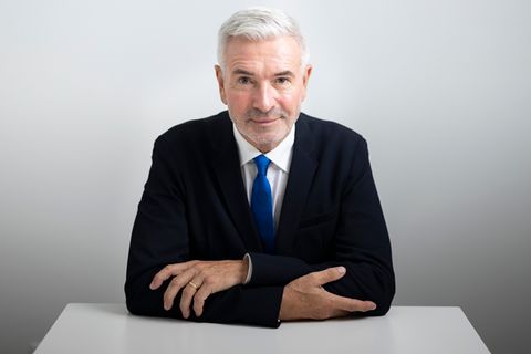 Roger Kusch lehnt mit verschränktem Armen an einem Schreibtisch und lächelt leicht
