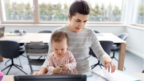 Eine Frau sitzt vor einem Laptop und hält ein Kleinkind auf dem Schoß