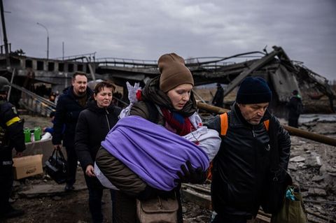 Menschen fliehen mit wenig Hab und Gut über eine zerstörte Brücke aus der ukrainischen Stadt Irpin