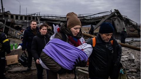 Menschen fliehen mit wenig Hab und Gut über eine zerstörte Brücke aus der ukrainischen Stadt Irpin