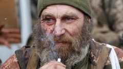Ein älterer weißer Mann mit grau-weiße Vollbart trägt Uniform und raucht eine Zigarette. Um sein rechtes Auge sind Wunden